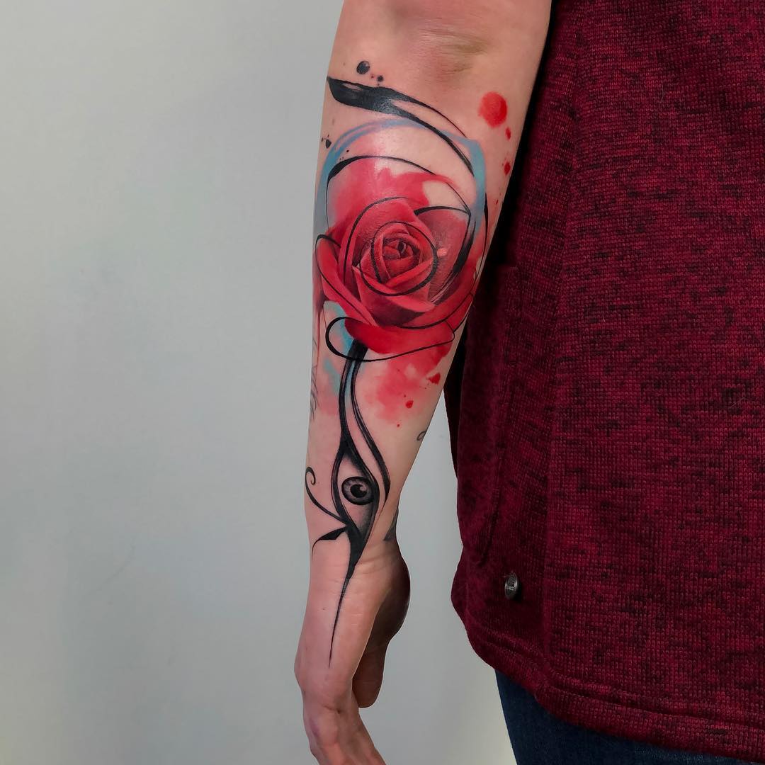 Antebrazo interior de una persona con un vibrante tatuaje de rosa roja, entretejido con líneas y formas abstractas negras y grises y salpicaduras rojas. La persona, que vestía una camisa granate, se hizo esta obra maestra en un reconocido estudio de Barcelona especializado en tatuajes únicos.